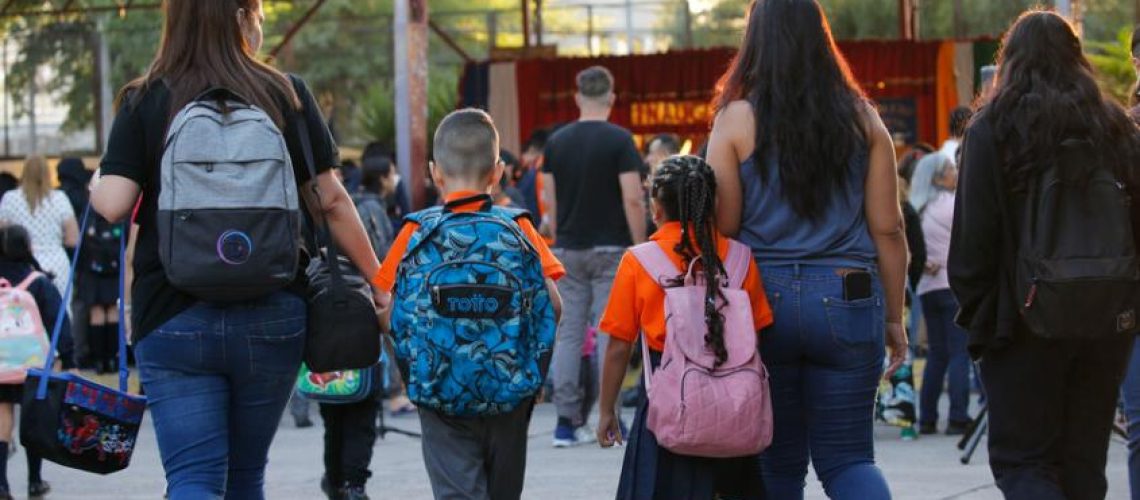 Foto de dos madres y sus dos hijos caminando hacia el ingreso de un colegio.